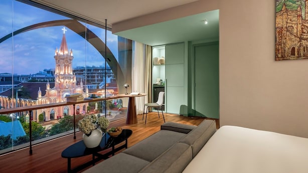 A modern hotel room with a large window offering a view of a historic church and cityscape. - M Village Hotel Đà Nẵng Centre, a brand of Modern Village Lifestyle (Da Nang)