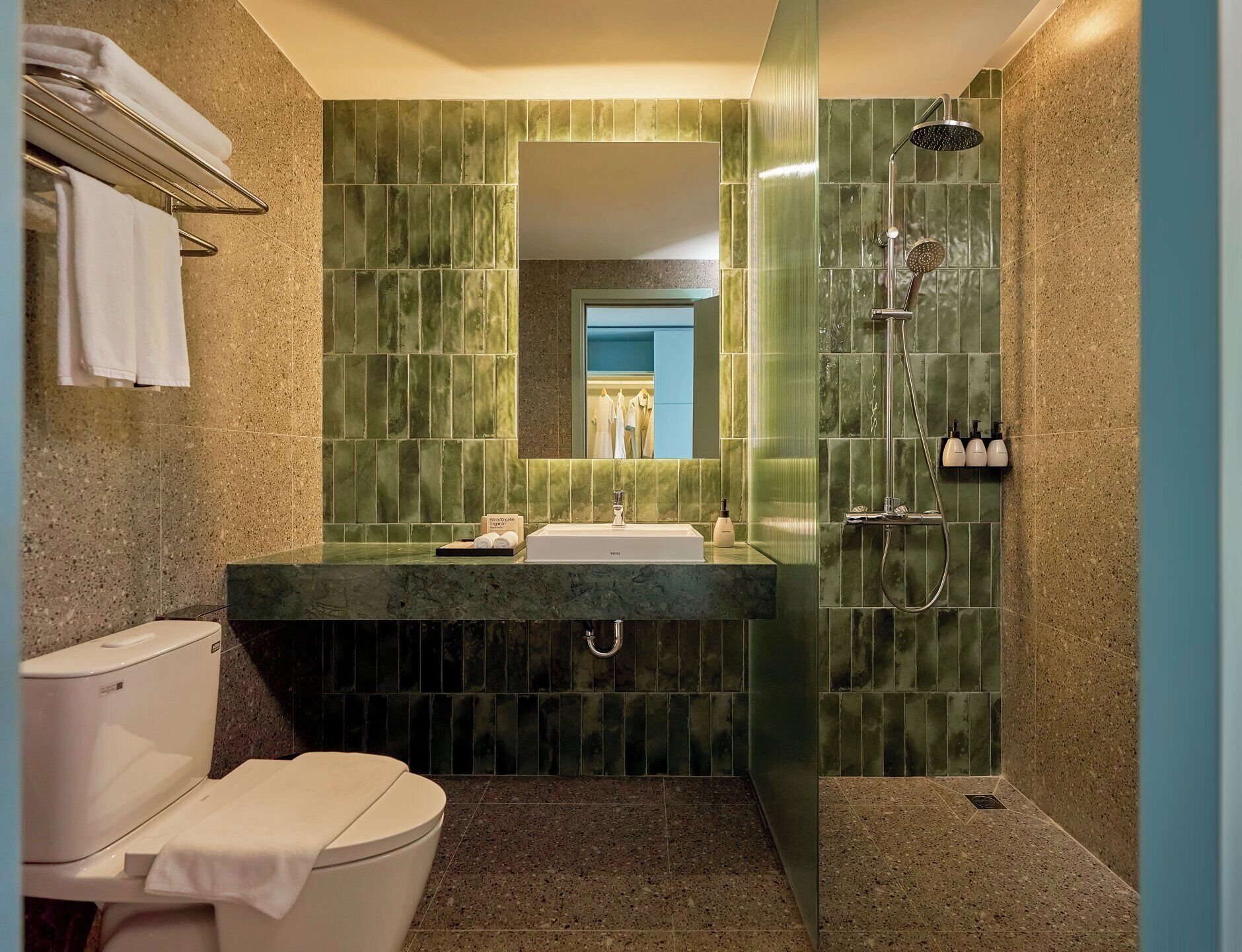 Un baño con ducha de azulejos verdes, un lavabo blanco y un inodoro.