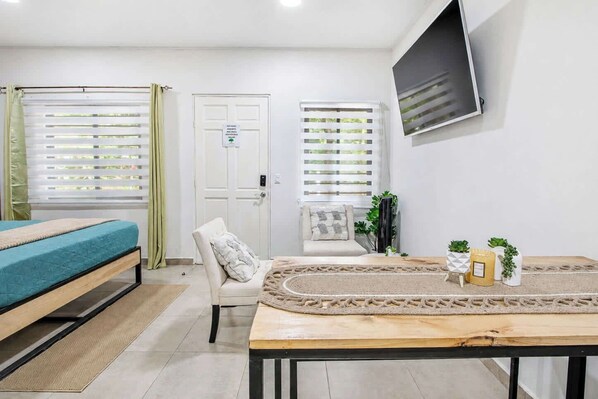 A bedroom with a bed, a chair, a table with plants, and a door with a sign.
