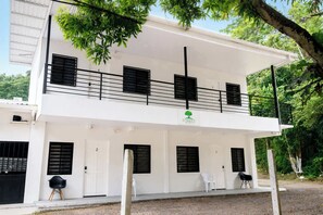A two-story building with a balcony, white walls, and black shutters.