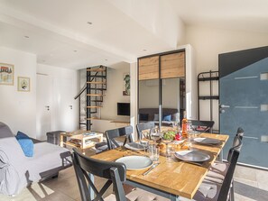 A dining area with a wooden table set for four, surrounded by chairs. A staircase with a wooden railing leads to an upper level. - Maison Fabrégas by Interhome (La Seyne Sur Mer, Les Sablettes)