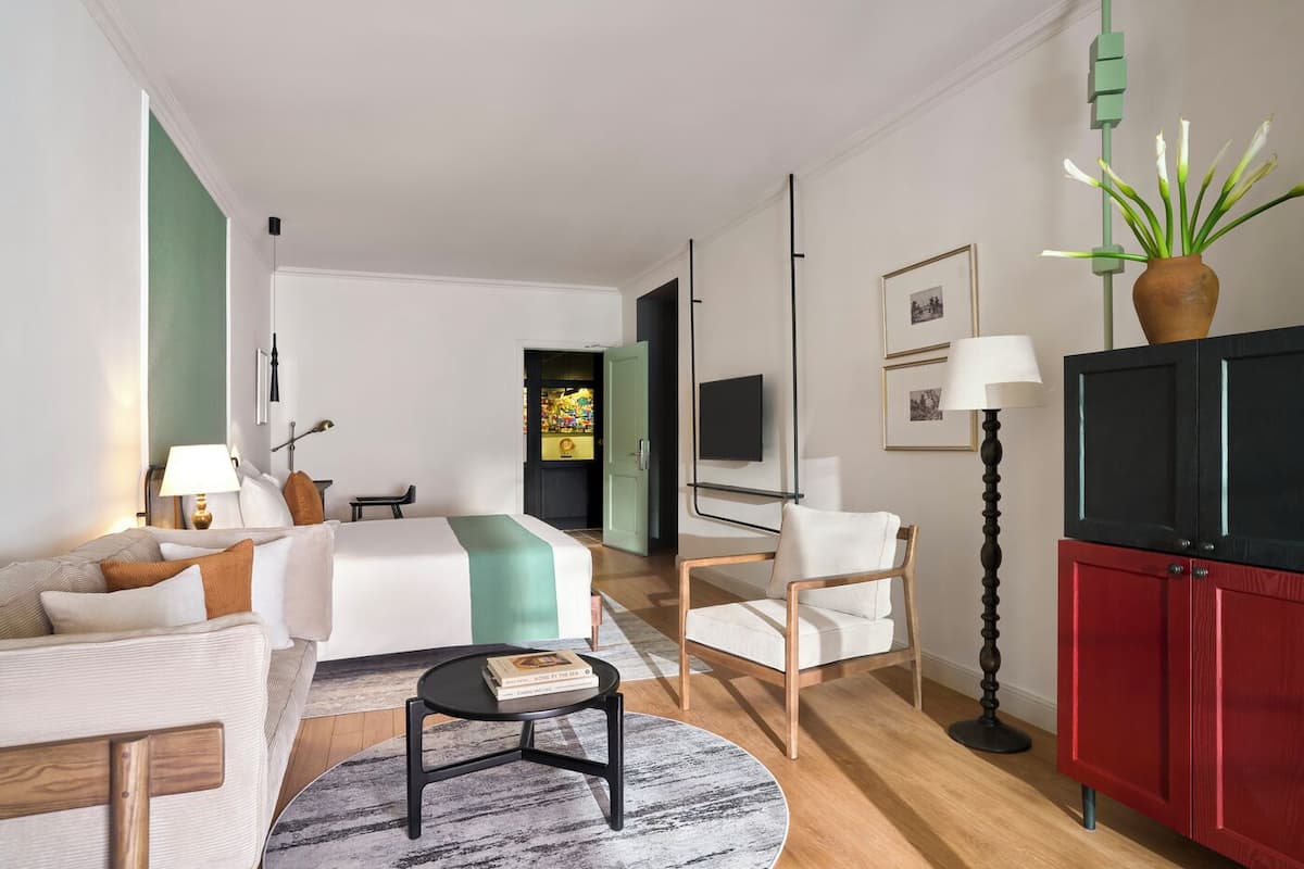Una habitación de hotel moderna con cama, sofá, escritorio, silla, televisor y armario.