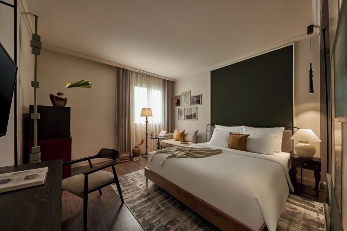 A hotel room with a large bed, a desk, a chair, a lamp, and a television.