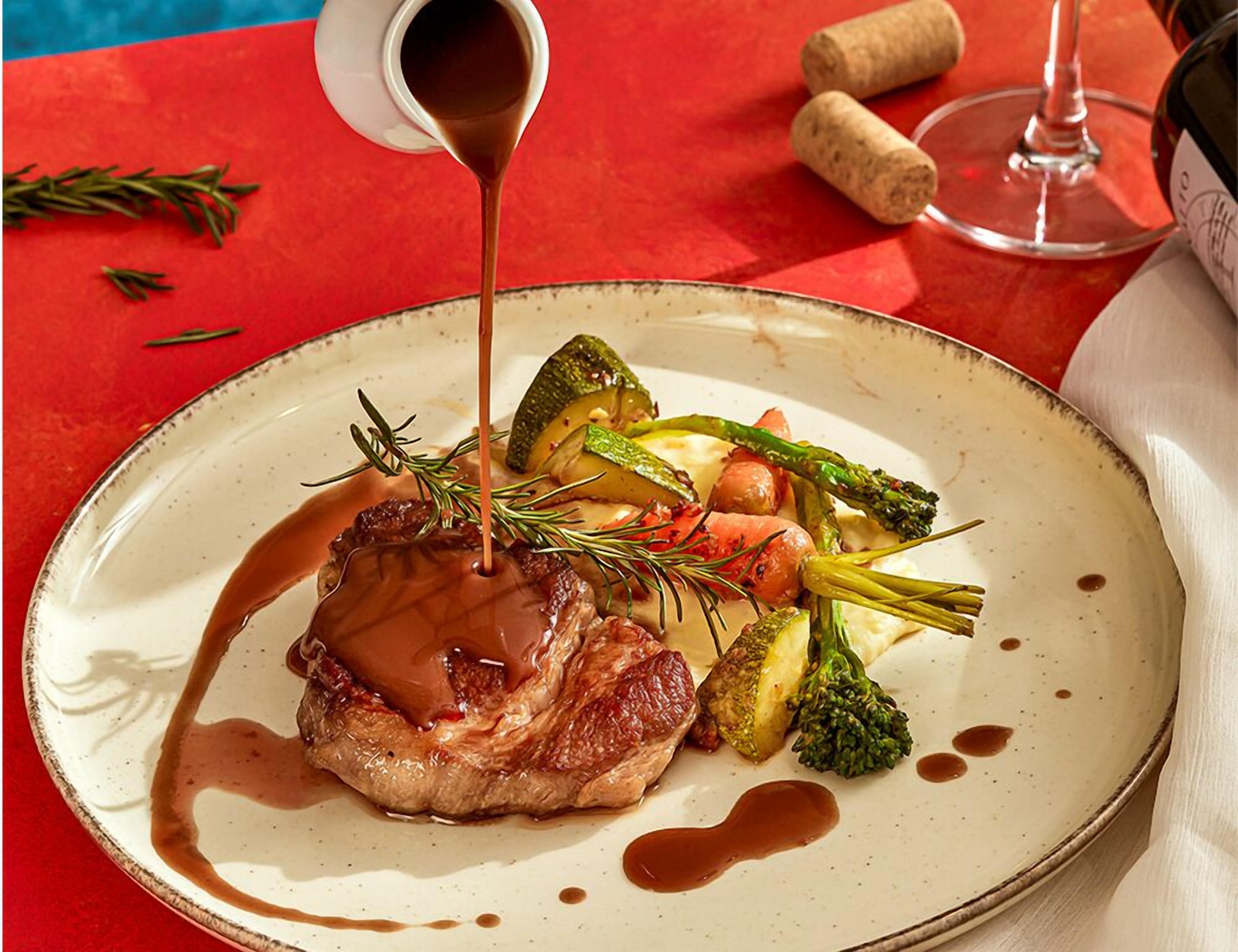 A plate of food with a sauce being poured over it, surrounded by vegetables and herbs.