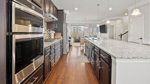 A modern kitchen with stainless steel appliances, wooden cabinets, and a large island. - 5-Star BWI Hanover 3-Level With Bonus Living Space (Hanover)