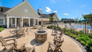 An outdoor patio with Adirondack chairs, a stone fire pit, and a pool in the background. - 5-Star BWI Hanover 3-Level With Bonus Living Space (Hanover)