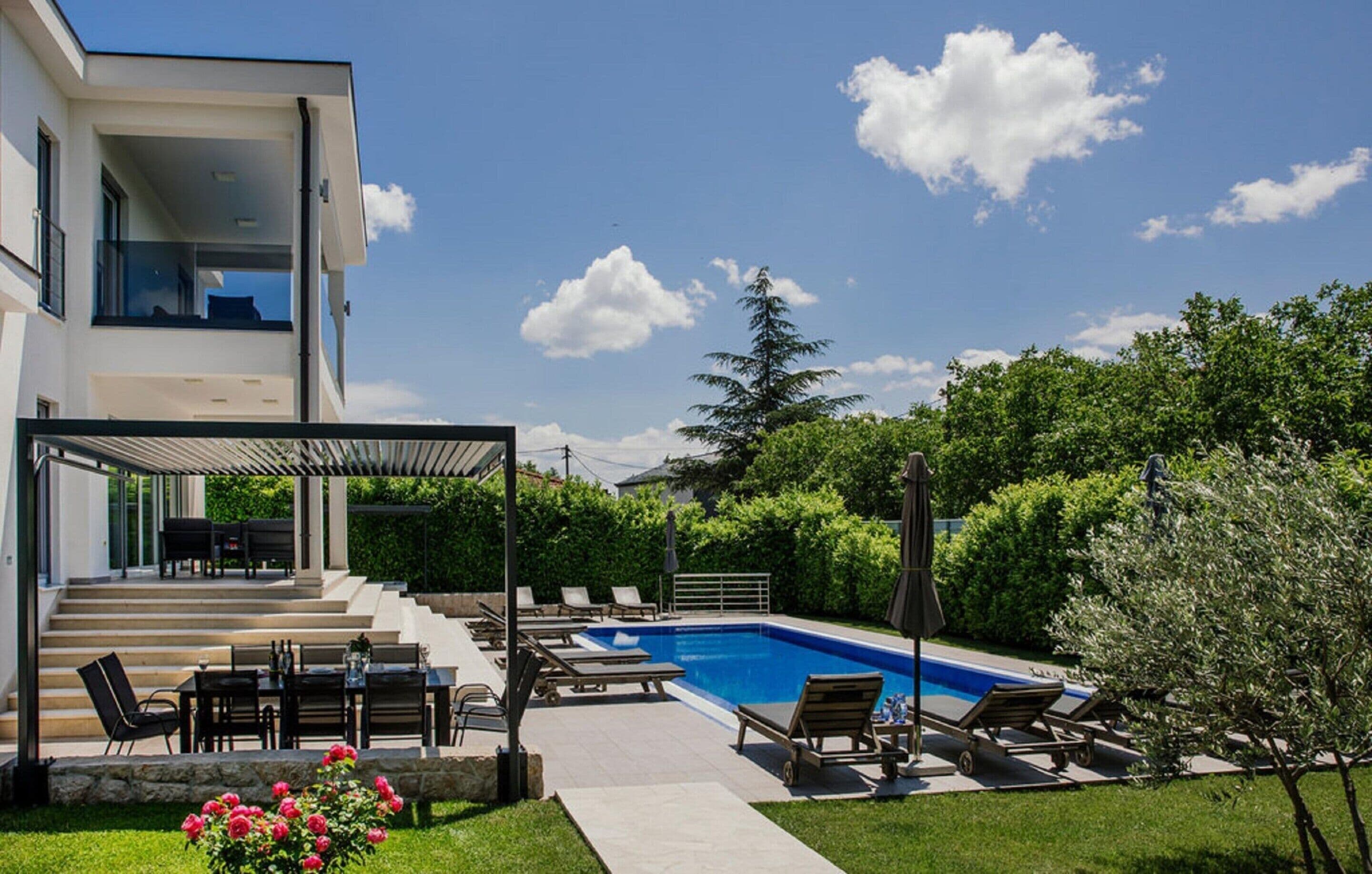Une maison moderne dotée d’une piscine, d’un espace salon extérieur et d’un patio couvert.