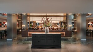 Eine moderne Hotelhalle mit Empfangstresen, einer Sitzecke und einer dekorativen Vase mit Blumen.