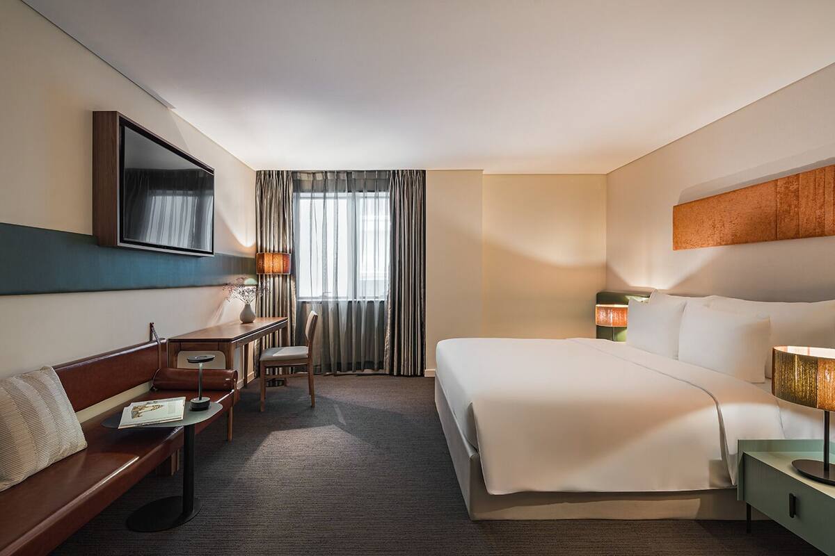 Une chambre d’hôtel avec un lit, un bureau, une chaise, une télévision et une fenêtre avec des rideaux.