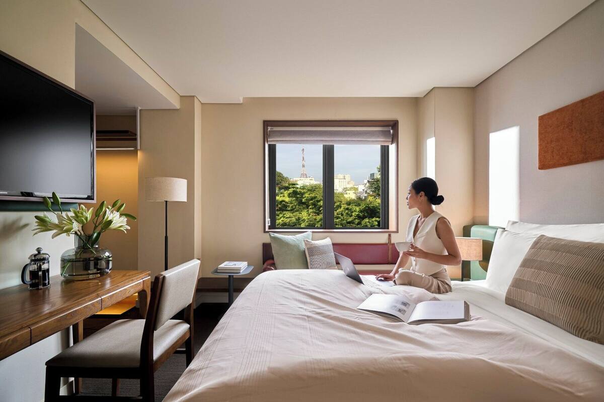 Une chambre d’hôtel équipée d’un lit, d’un bureau, d’une chaise, d’une télévision et d’une fenêtre donnant sur la ville.