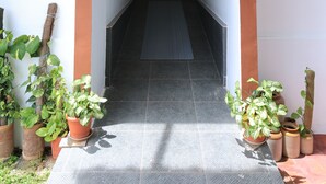 A hallway with a door at the end, flanked by potted plants and a tiled floor. - Iyer Square (Mannarkkad)
