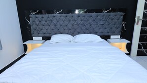 A modern bedroom with a tufted headboard, white bedding, and bedside lamps. - Iyer Square (Mannarkkad)