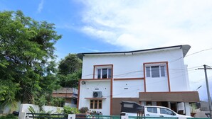 A two-story house with a white exterior and brown trim, a car parked in front, and a green fence. - Iyer Square (Mannarkkad)