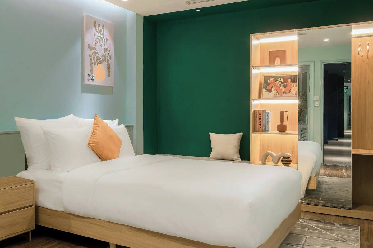 A modern bedroom with a large bed, a nightstand, a bookshelf, and a mirror.