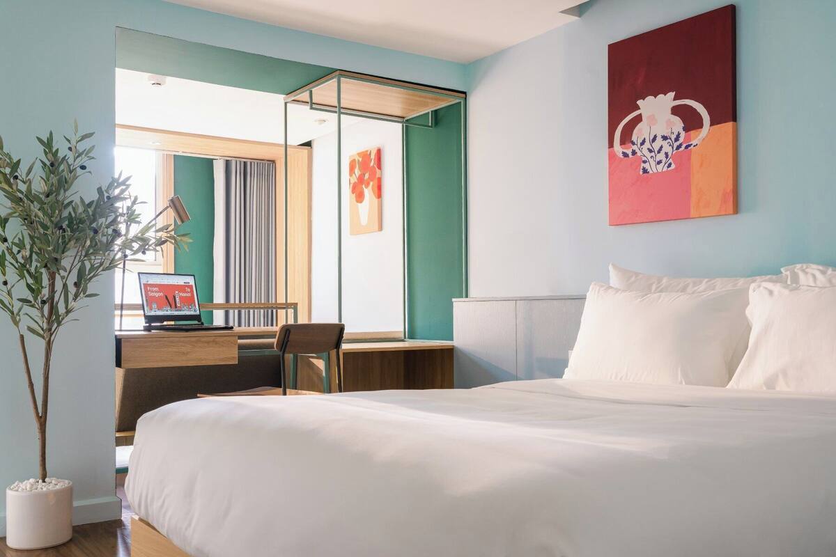 A hotel room with a bed, a desk, a chair, and a potted plant.