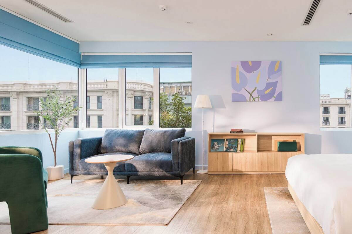A modern hotel room with a sofa, a small round table, a wooden cabinet, and a bed.