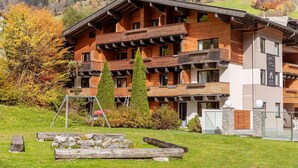 Un immeuble en bois à plusieurs étages, doté de balcons, entouré d’un feuillage automnal et d’une pelouse avec une aire de jeux comprenant une balançoire.