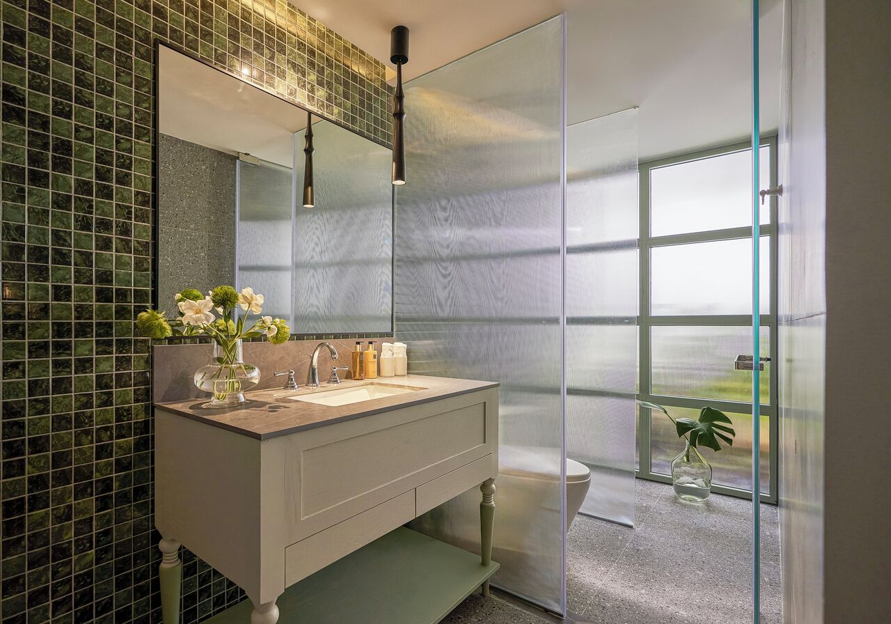 Un baño moderno con un espejo grande, un lavamanos y un inodoro. Hay una ventana con vistas al exterior.
