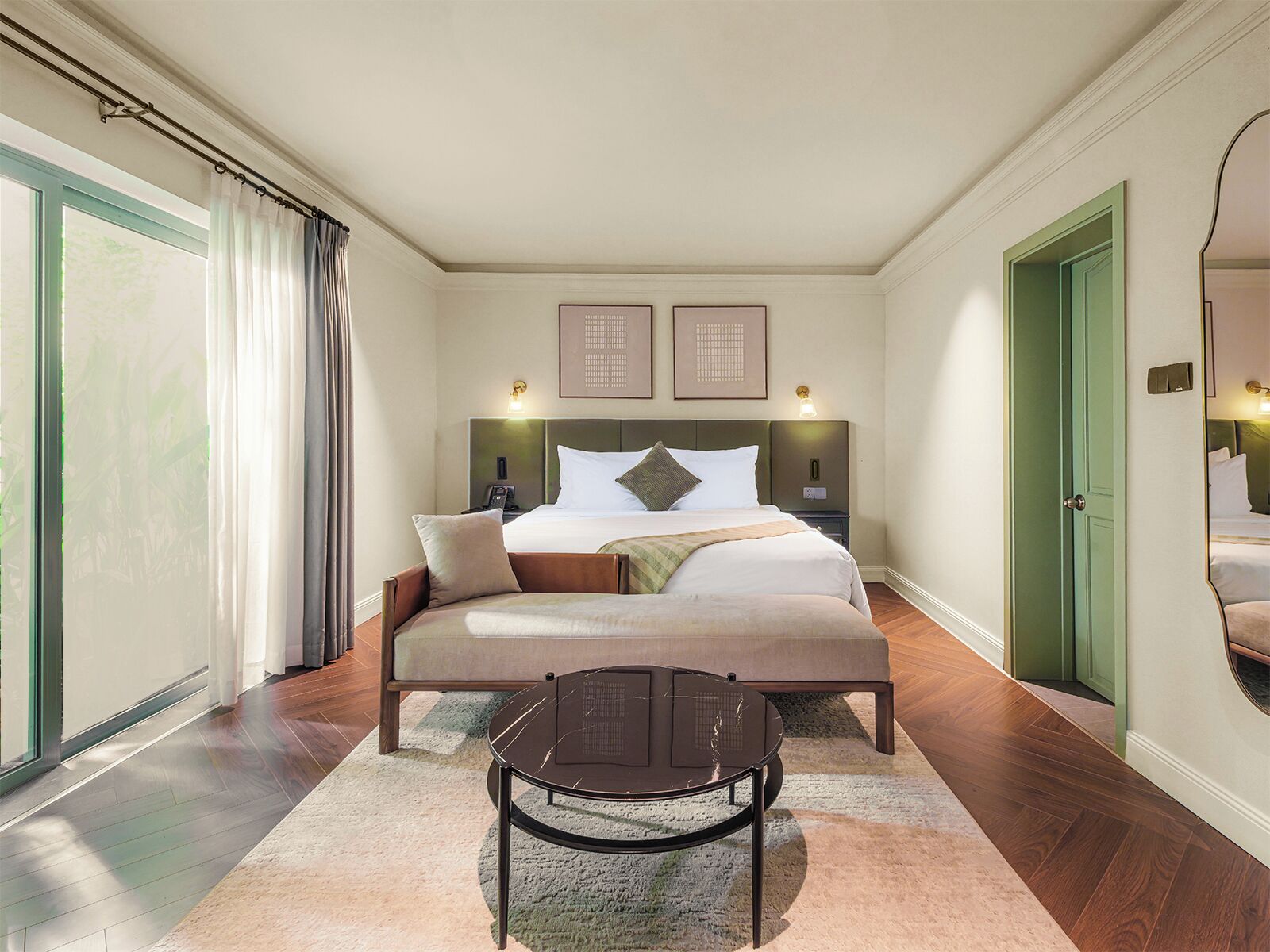 Una habitación de hotel con cama, mesitas de noche, una silla, un ventanal con cortinas y una puerta.