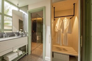Une salle de bain moderne avec un meuble-lavabo, un grand miroir et un dressing où sont suspendus des peignoirs.