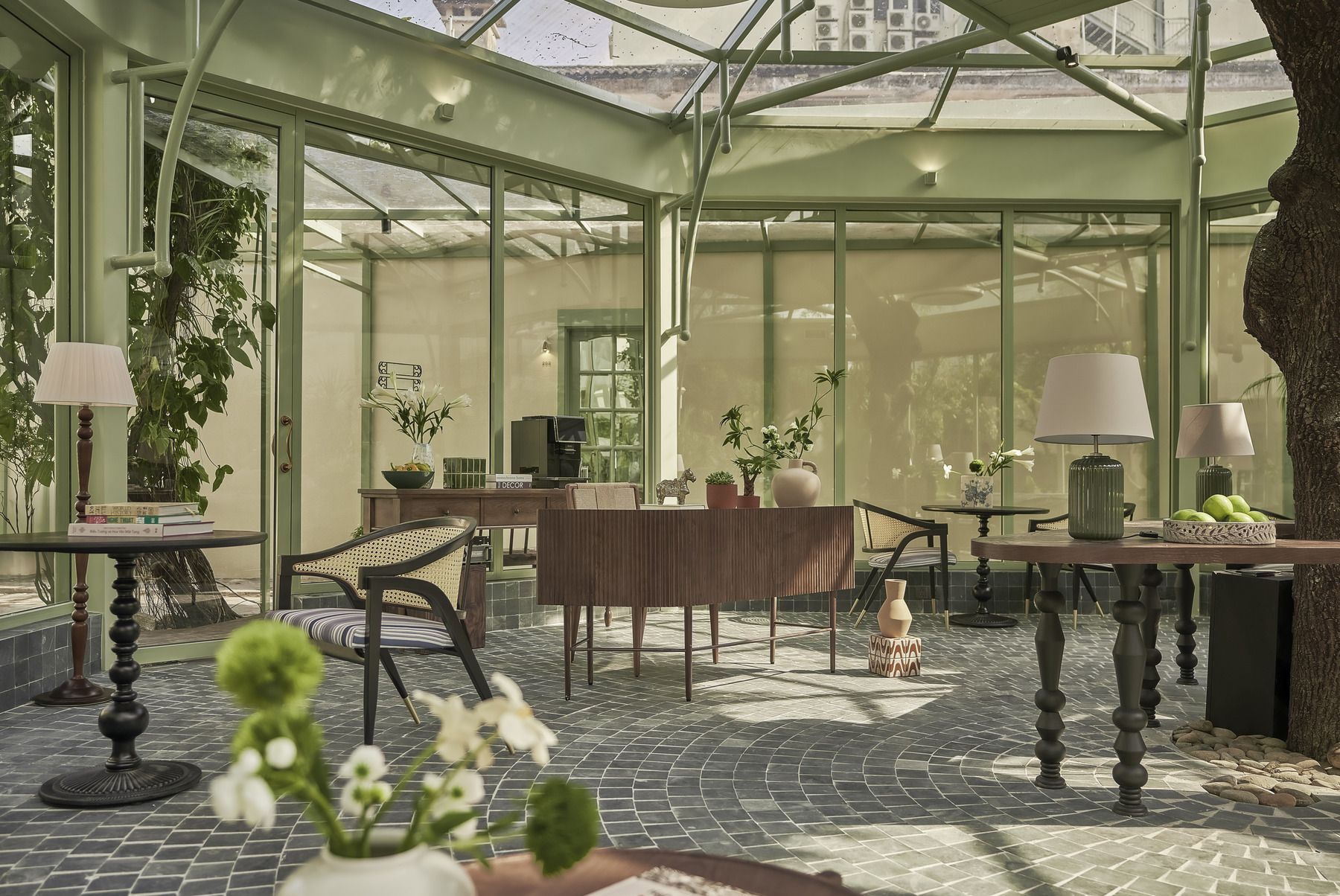 Une véranda dotée d’un toit en verre, aménagée avec des tables, des chaises et des plantes en pot.
