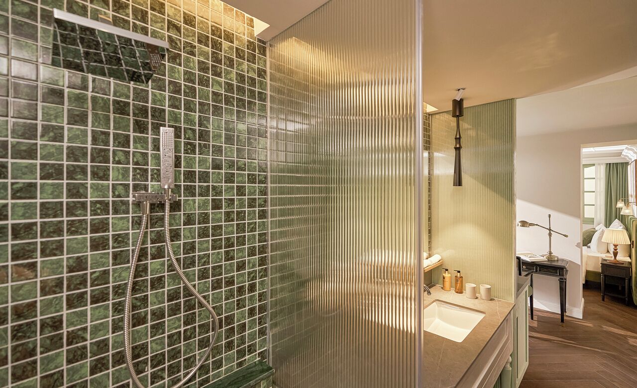 Une salle de bain avec une douche carrelée de mosaïques vertes, un lavabo avec un miroir et une petite table avec une lampe.