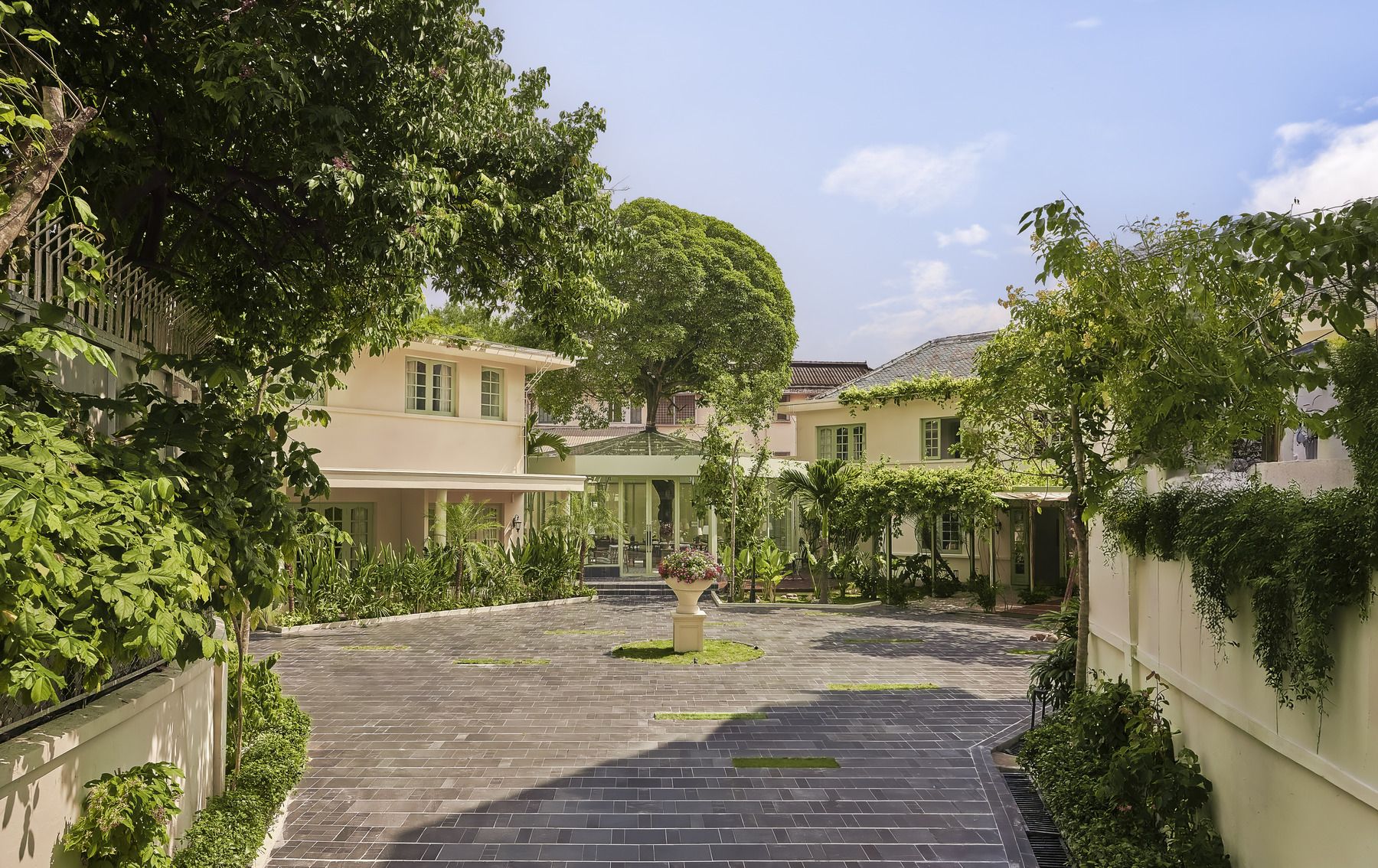 A courtyard with a paved walkway, surrounded by lush greenery and buildings with multiple windows.