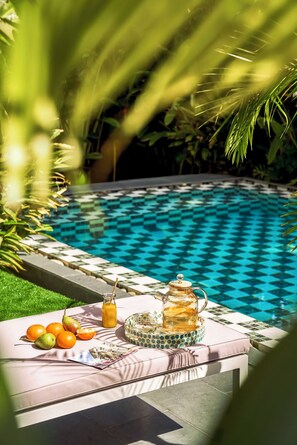 Ein Poolbereich mit Tisch, der für Tee und Obst gedeckt ist, umgeben von üppiger Vegetation.