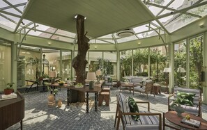 A conservatory with a central tree, seating areas, and potted plants. - President Maison Signature by M Village, a brand of Modern Village Lifestyle (Ho Chi Minh City)