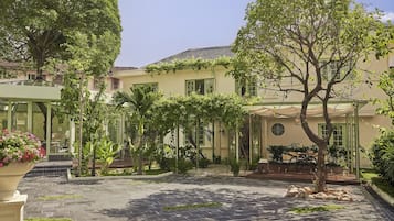 A courtyard with a paved walkway, surrounded by lush greenery and a building with a tiled roof.