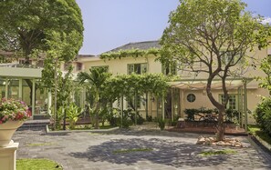 A courtyard with a paved walkway, surrounded by lush greenery and a building with a tiled roof. - President Maison Signature by M Village, a brand of Modern Village Lifestyle (Ho Chi Minh City)