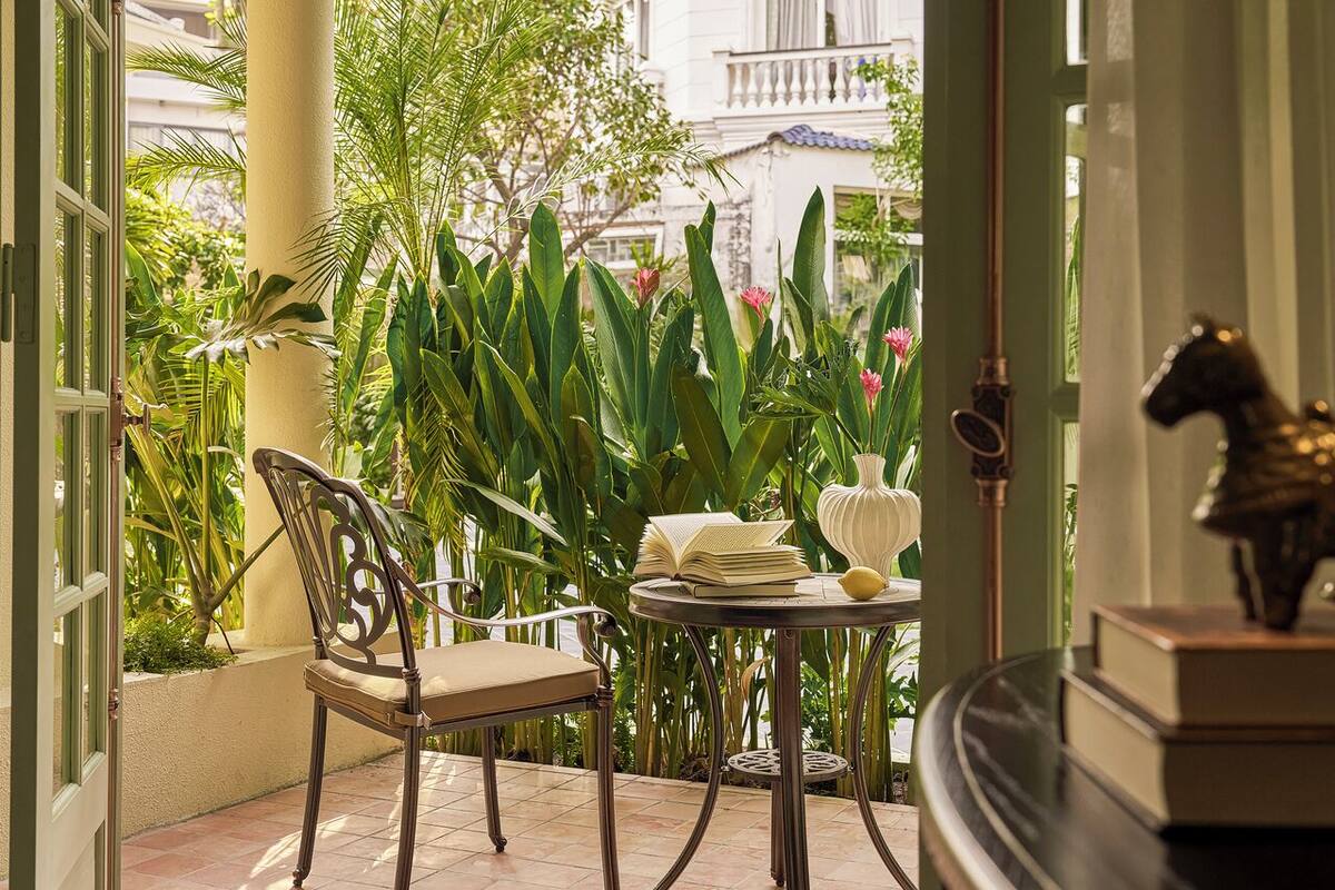 A cozy outdoor seating area with a chair and a table, surrounded by lush greenery and a view of a building.