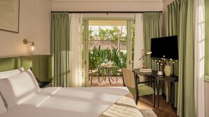 A hotel room with a large bed, a desk with a TV, and a view of a garden through an open door. - President Maison Signature by M Village, a brand of Modern Village Lifestyle (Ho Chi Minh City)