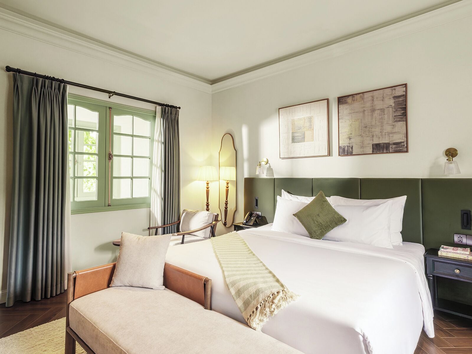 Ein Hotelzimmer mit Bett, Sessel, Nachttisch, Lampe und zwei gerahmten Bildern an der Wand.