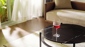 A room with a bed, a round table with a glass of red wine, and a view of greenery through a window. - President Maison Signature by M Village, a brand of Modern Village Lifestyle (Ho Chi Minh City)