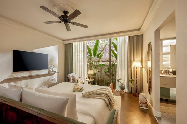 Une chambre d’hôtel avec un lit, une télévision, un ventilateur de plafond, une fenêtre avec des rideaux et une salle de bain visible à travers une porte ouverte.