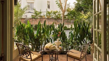 A balcony with a table, chairs, and a view of a building and greenery.