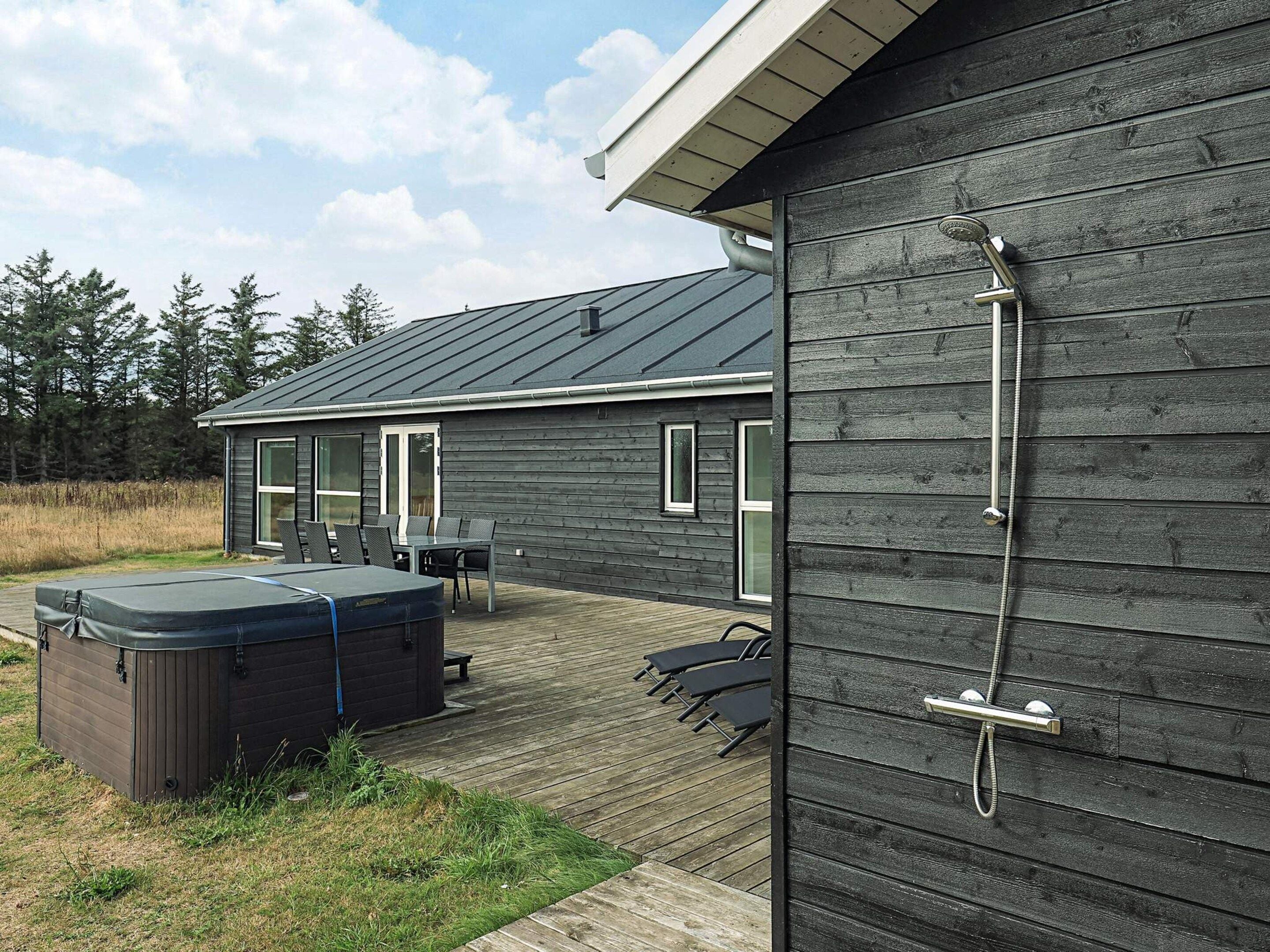 Una terraza de madera con un jacuzzi, asientos exteriores y una ducha.