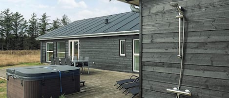 A wooden deck with a hot tub, outdoor seating, and a shower.