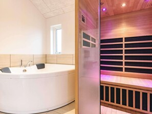 A modern bathroom with a large bathtub, a window, and a sauna area. - 4 Star Holiday Home in Lokken (Lokken)