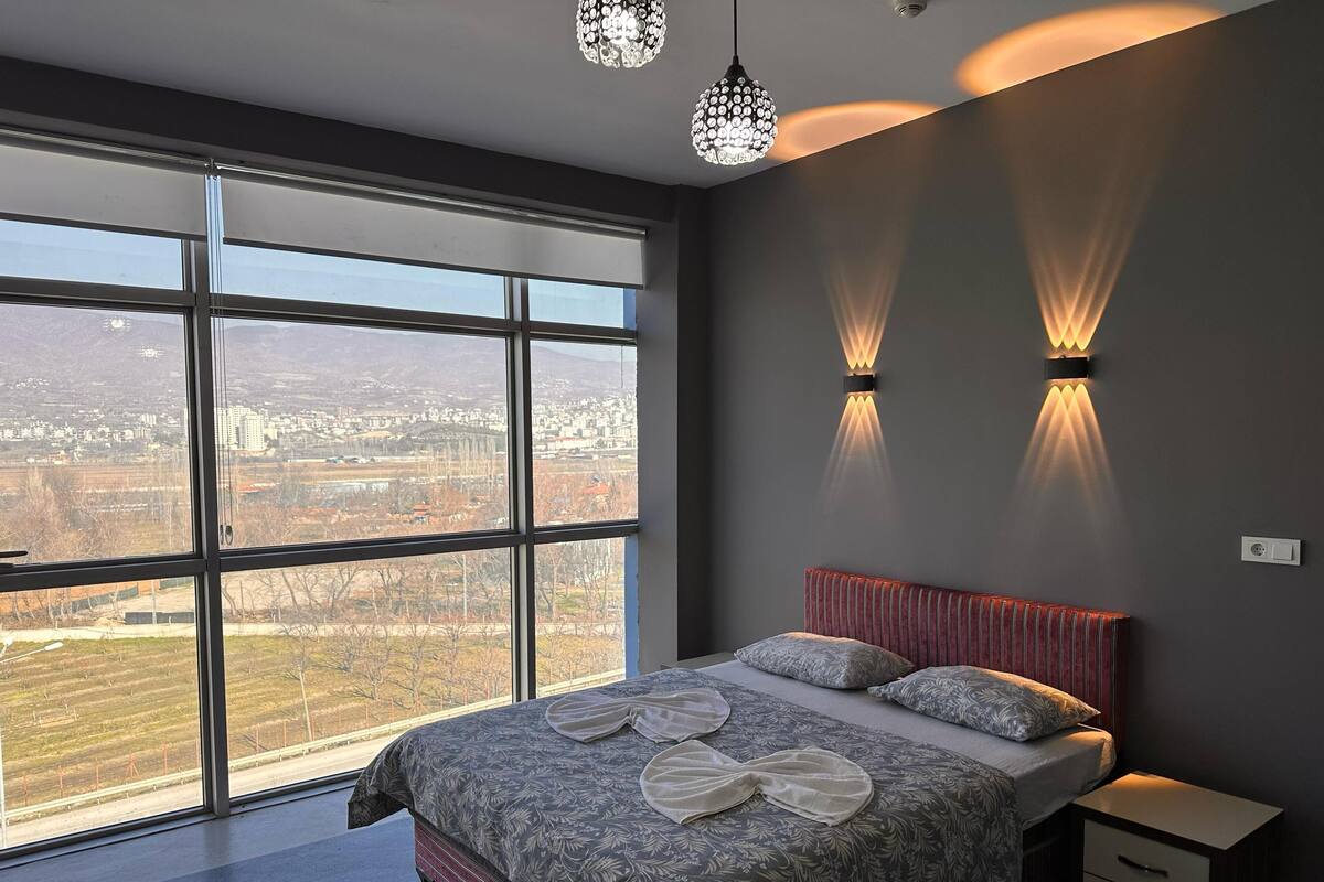 A bedroom with a large window, a bed with floral bedding, two wall-mounted lights, and a nightstand.