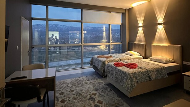 Un dormitorio moderno con un ventanal grande, dos lámparas de noche, un escritorio y una alfombra estampada.