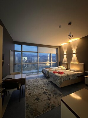 A modern bedroom with a large window, two bedside lamps, a desk, and a patterned rug. -  Pasha Plus Hotel (Tokat)