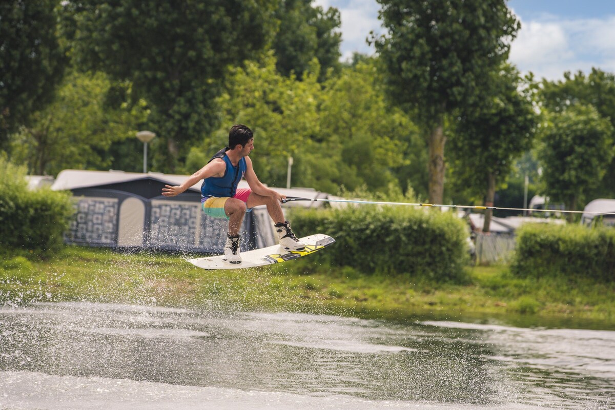 A person wakeboarding on a body of water with trees and a building in the background.