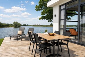A deck with a table and chairs overlooking a lake, with a modern building adjacent to the deck.