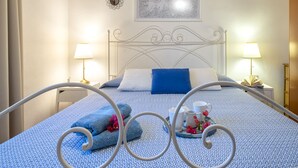 Een net opgemaakt bed met een blauw-wit gebed eilandhoes, twee nachtlampjes, een ingelijste afbeelding boven het bed, en een decoratieve schaal met een kopje en bloemen op het bed.