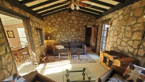 Una habitación con paredes de piedra, un ventilador de techo, un sofá, una mesa de centro de vidrio y una alfombra de piel.