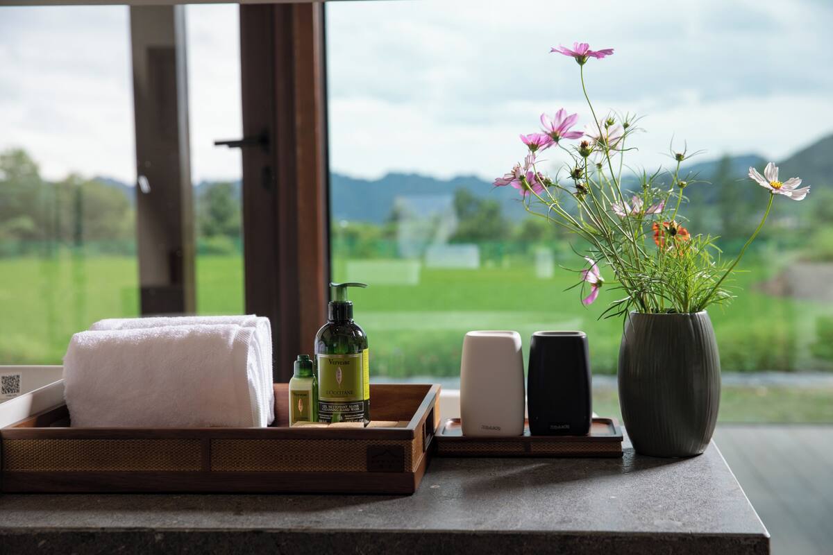 Ein Badezimmer-Anschlag mit Handtuch, Pflegeprodukten und einer Blumenvase.