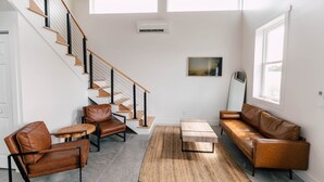 A modern living room with a staircase, leather furniture, and large windows. - Riverbend Ranch Cabin #1 (Normandy)