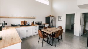 A modern kitchen with white cabinets, a wooden countertop, and a dining area with a wooden table and chairs. - Riverbend Ranch Cabin #1 (Normandy)